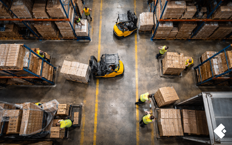 A claims investigator documenting forklift incident evidence on a warehouse floor as part of a manufacturing workers compensation investigation during spring peak season.